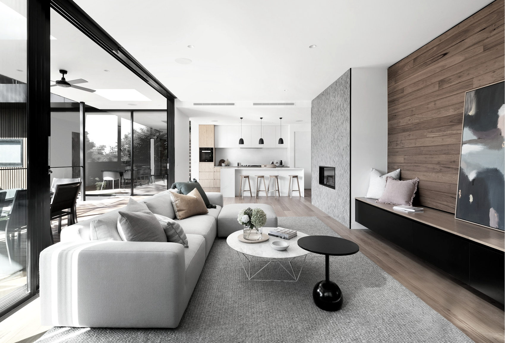 Living room with a concrete chimney breast, timber wall and sliding glazing open to a terrace